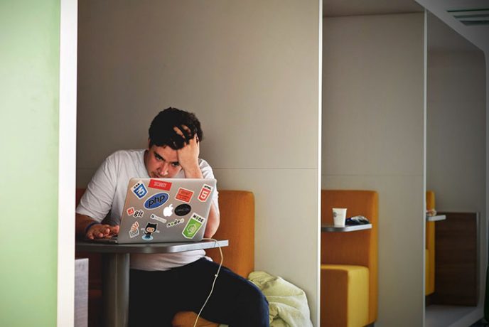 Ein gestresster Mann, der neben einem Computer in einem Café sitzt. Die Vorbereitung Deines Affiliate-Business auf die Angebote-Saison kann schwierig sein, da der Druck besteht, Einnahmen zu erzielen.